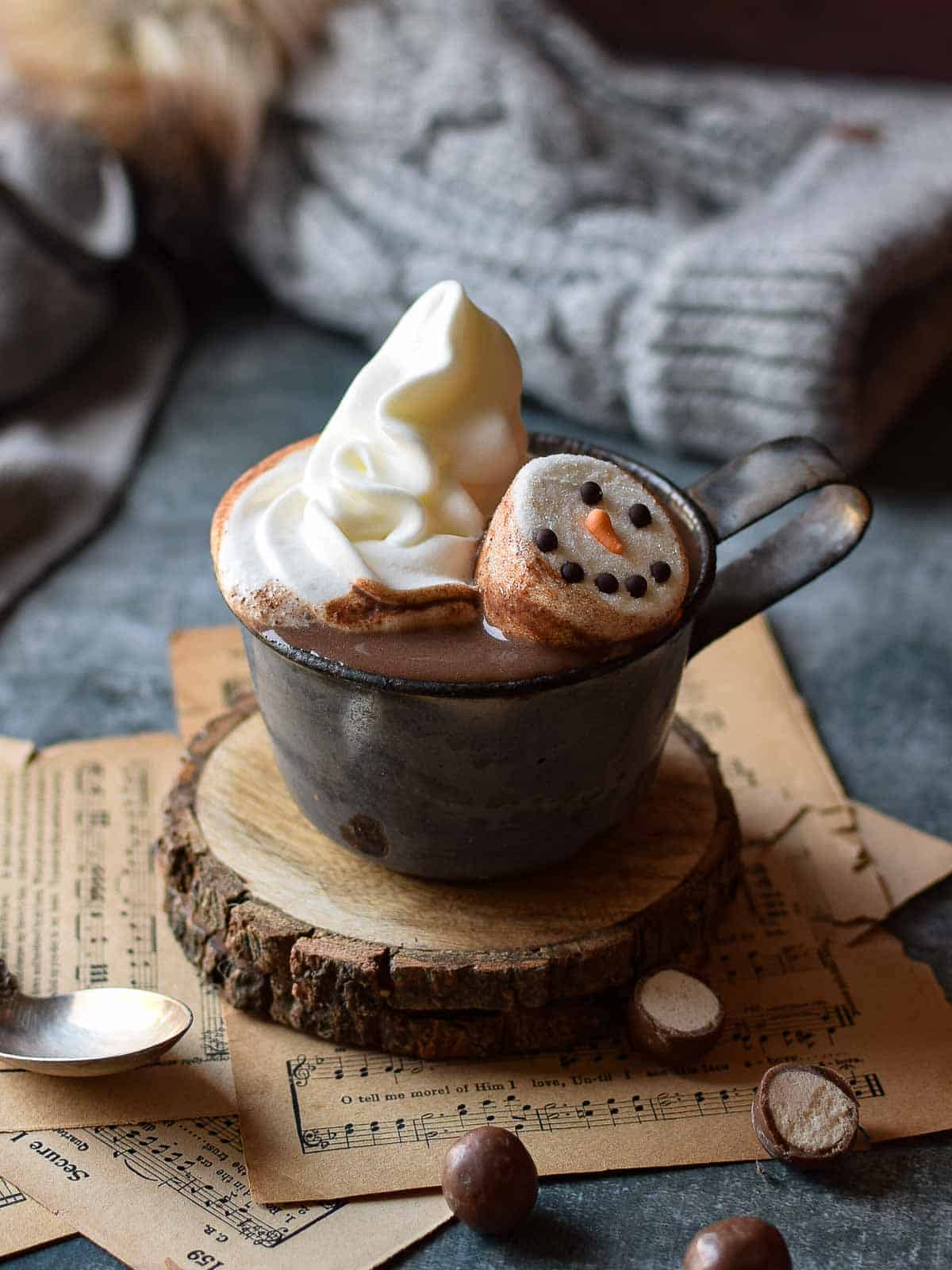 Malted milk hot chocolate in a grey mug with whipped cream and snowman marshmallows.