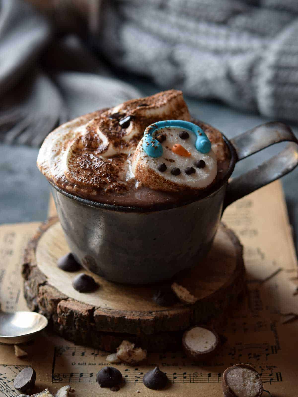 Malted milk hot chocolate in a grey mug with whipped cream and snowman marshmallows.