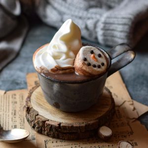 Malted milk hot chocolate in a grey mug with whipped cream and snowman marshmallows.