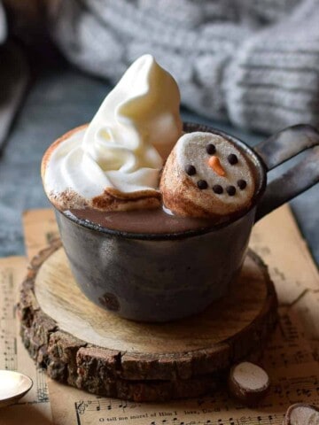 Malted milk hot chocolate in a grey mug with whipped cream and snowman marshmallows.
