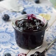 Close-up of blueberry earl grey jam on blue tile in a small glass jar.