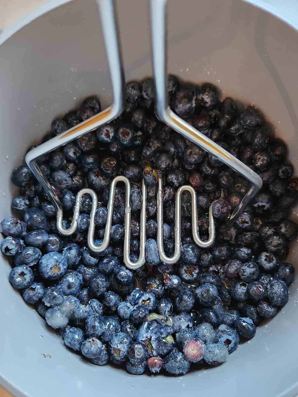 Mashing blueberries and sugar in a pot for making jam.