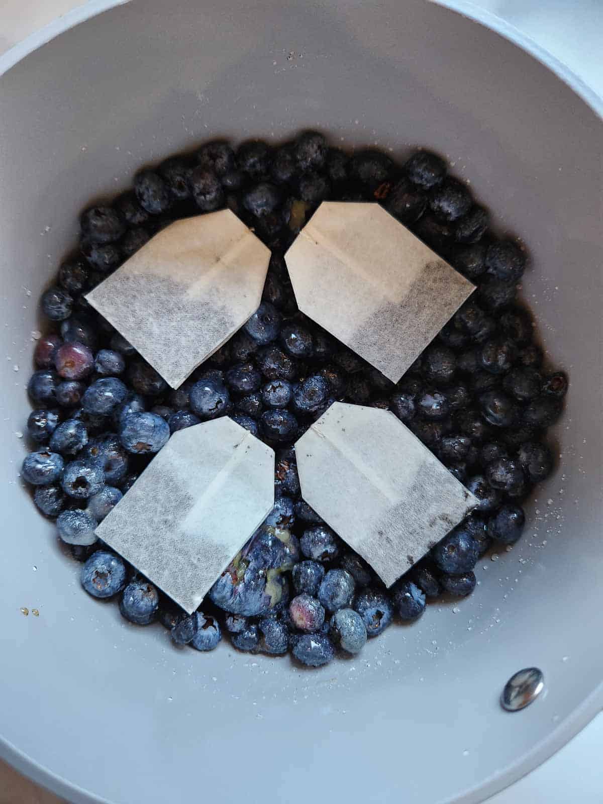 Earl grey tea bags added to blueberry jam in a pot.