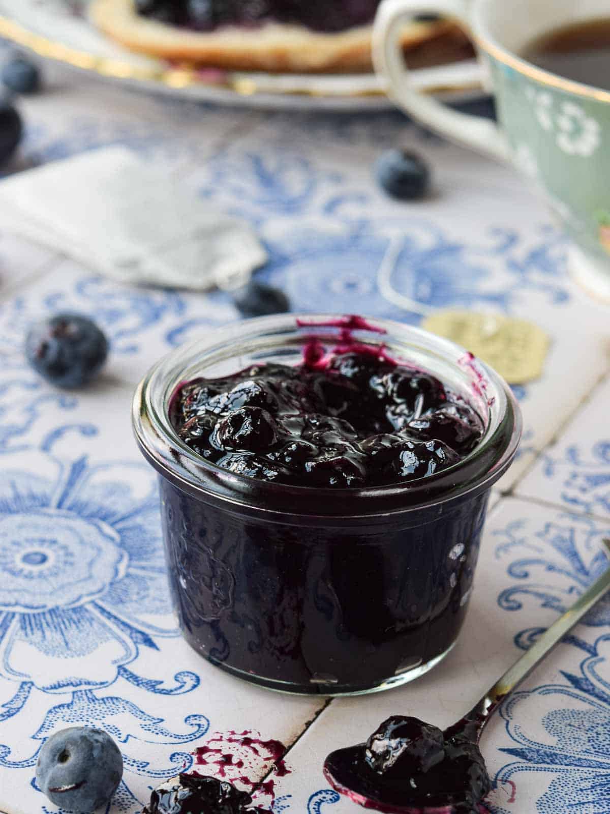 Close-up of blueberry earl grey jam on blue tile in a small glass jar.
