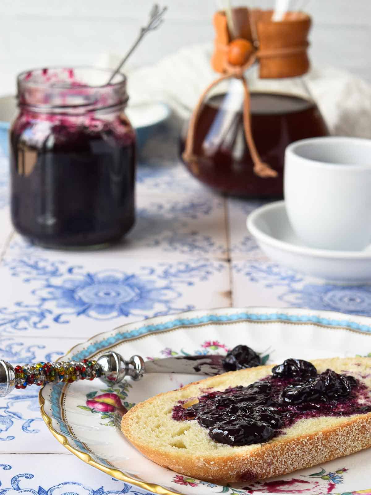 Blueberry earl grey jam spread on toast with coffee in the background.