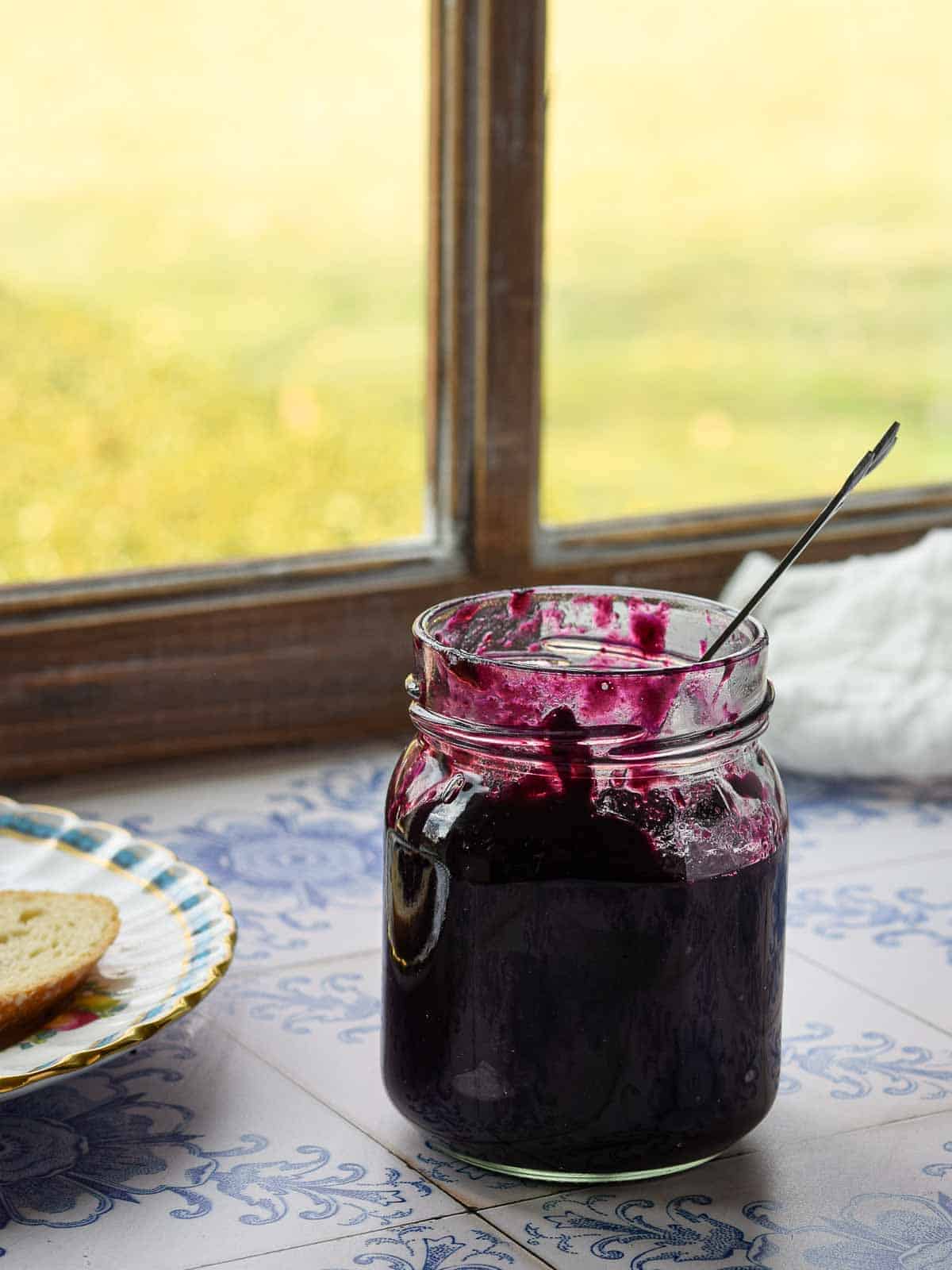 Blueberry earl grey jam in a glass jar by the window with light coming in.