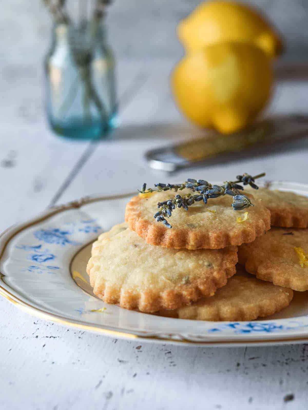 Lemon lavender shortbread cookies stacked on top of a floral plate on a wood background.