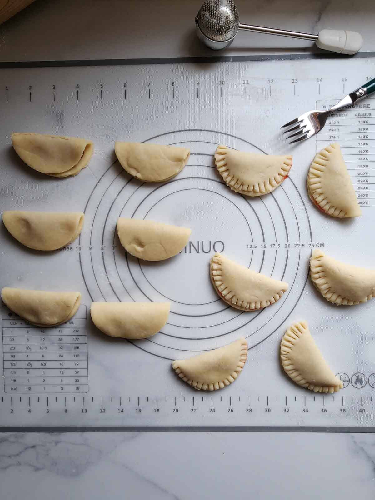 Pie dough circles folded in half and being crimped with a fork for making mini pies.