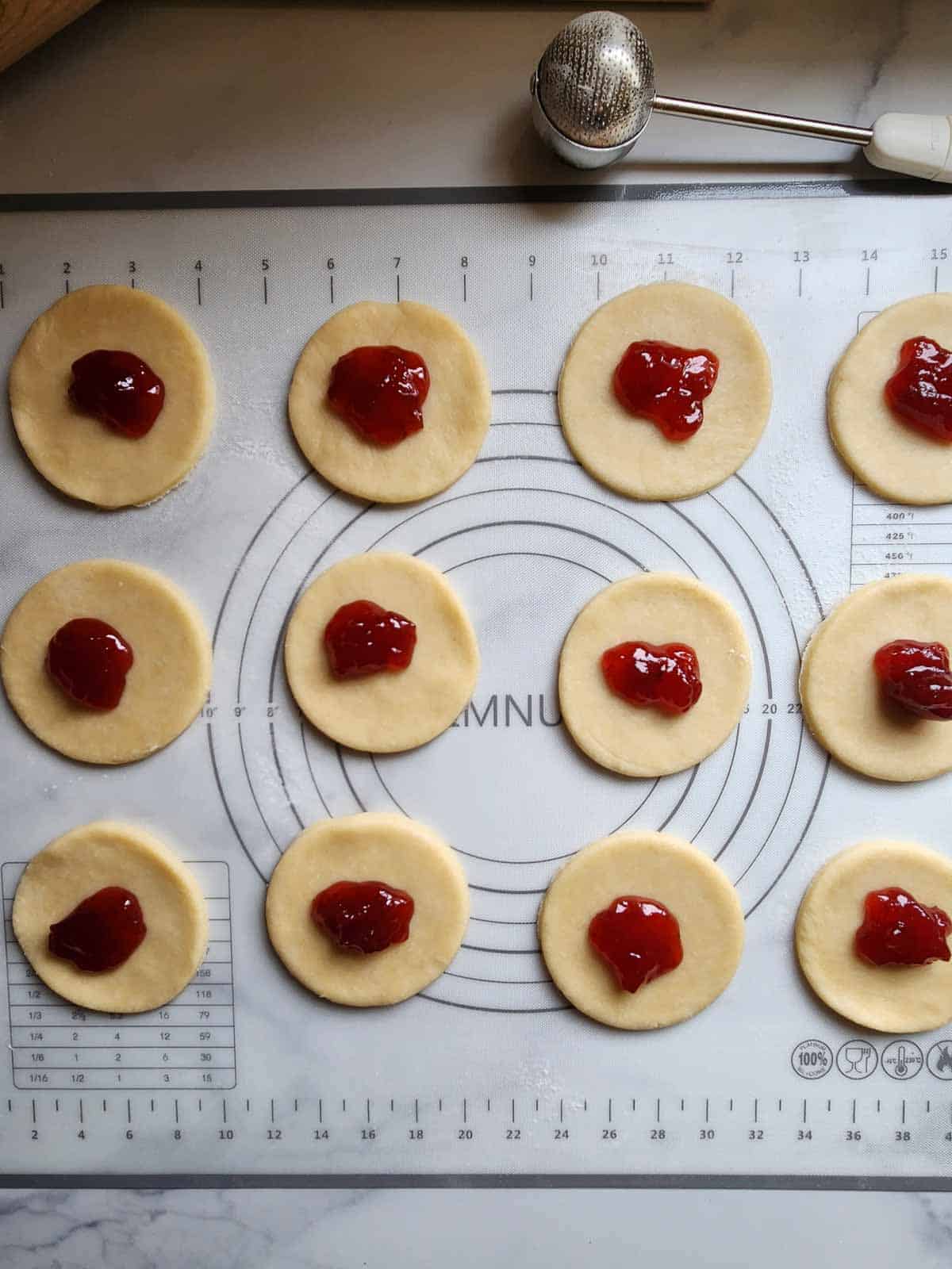 Pie dough cut in circles with strawberry jam placed in the middle.