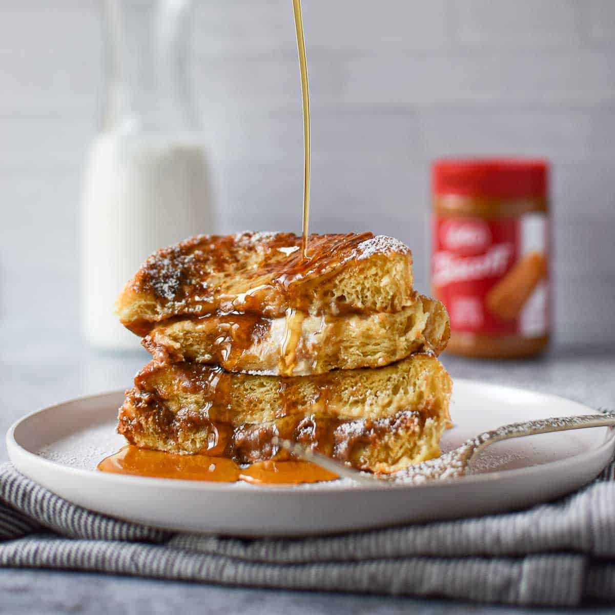 Stuffed French toast on a white plate, with maple syrup drizzled over it.