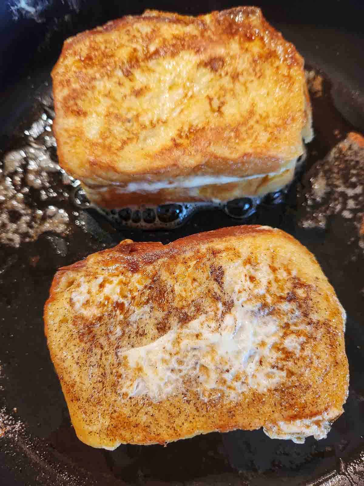 Stuffed French toast cooking on a buttered griddle.