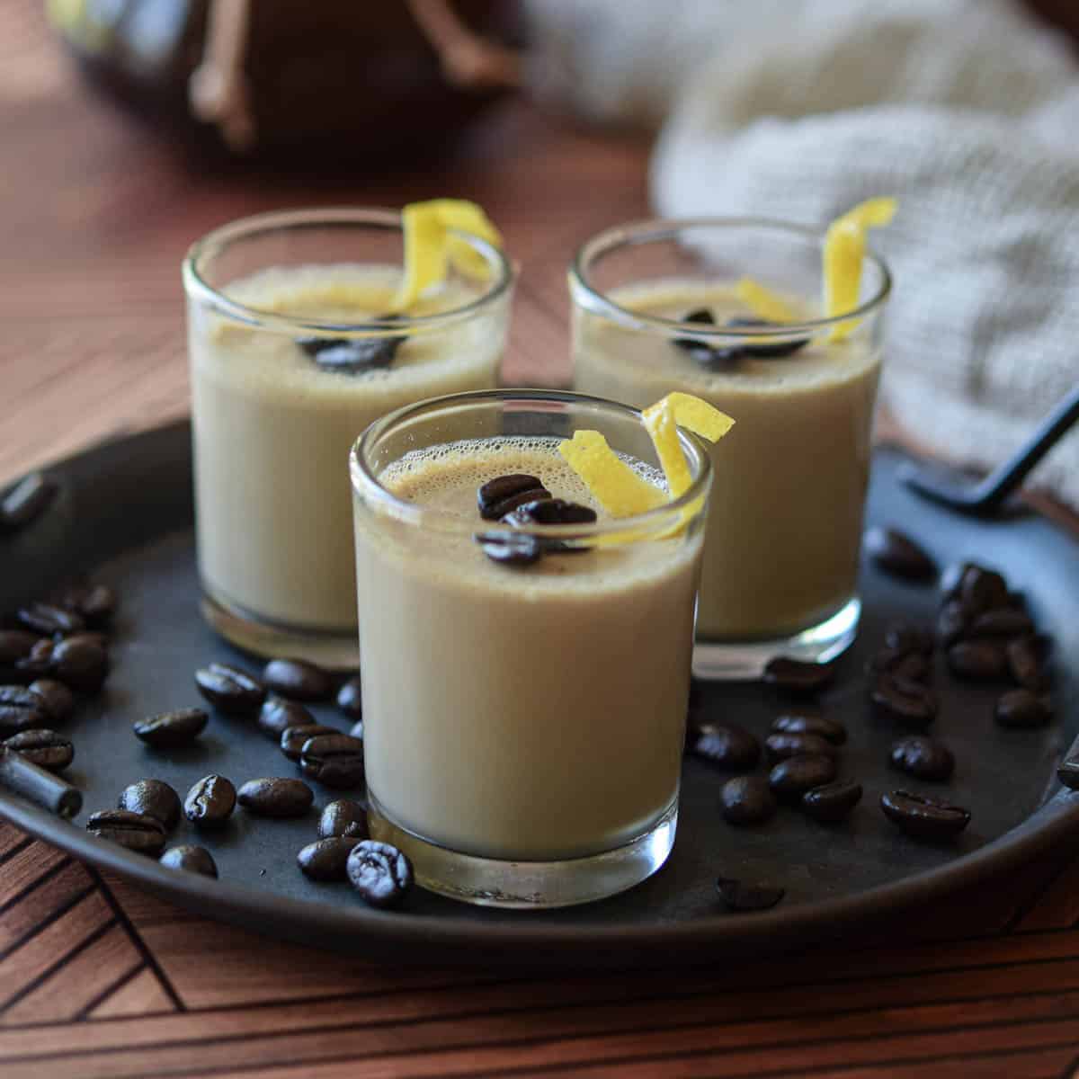 Espresso panna cotta in mini clear cups with coffee beans scattered around it on a wood surface.