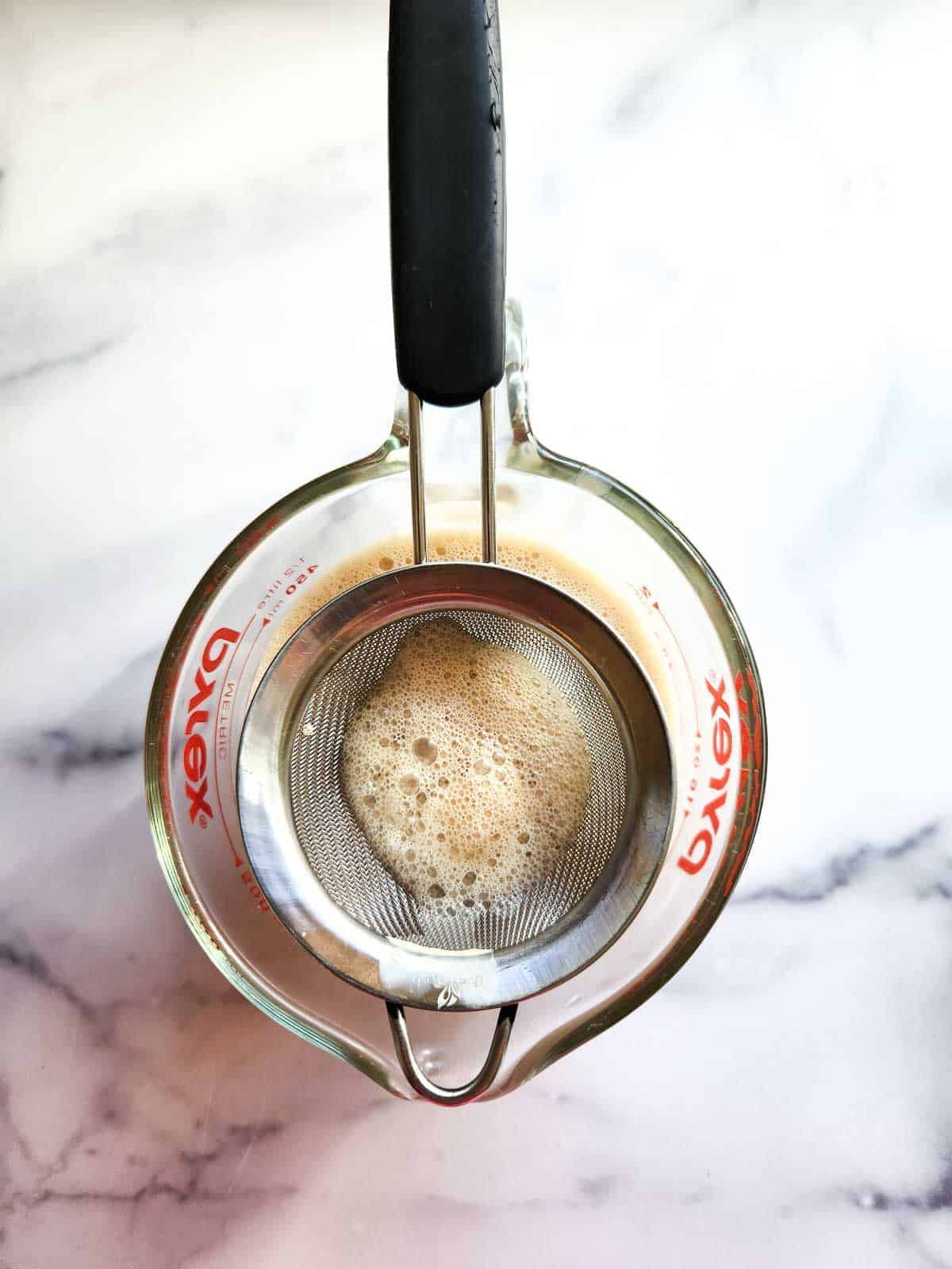 Straining espresso panna cotta liquid into a cup.