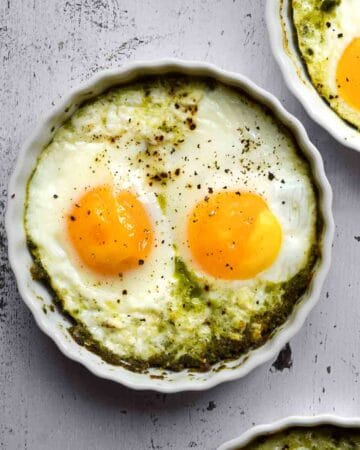 Overhead view of baked eggs in ramekins with pesto,