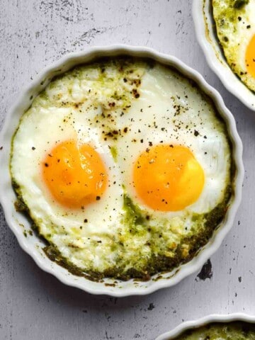 Overhead view of baked eggs in ramekins with pesto,