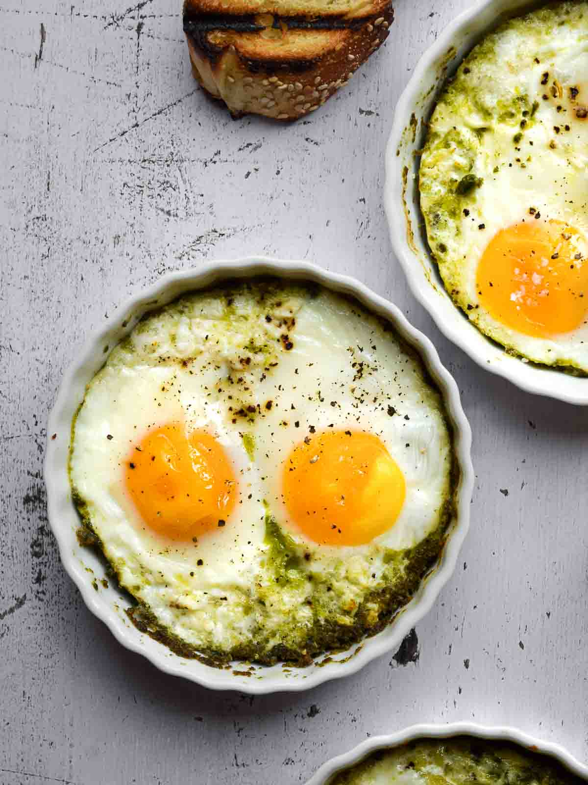 Overhead view baked eggs with pesto in white ramekins.