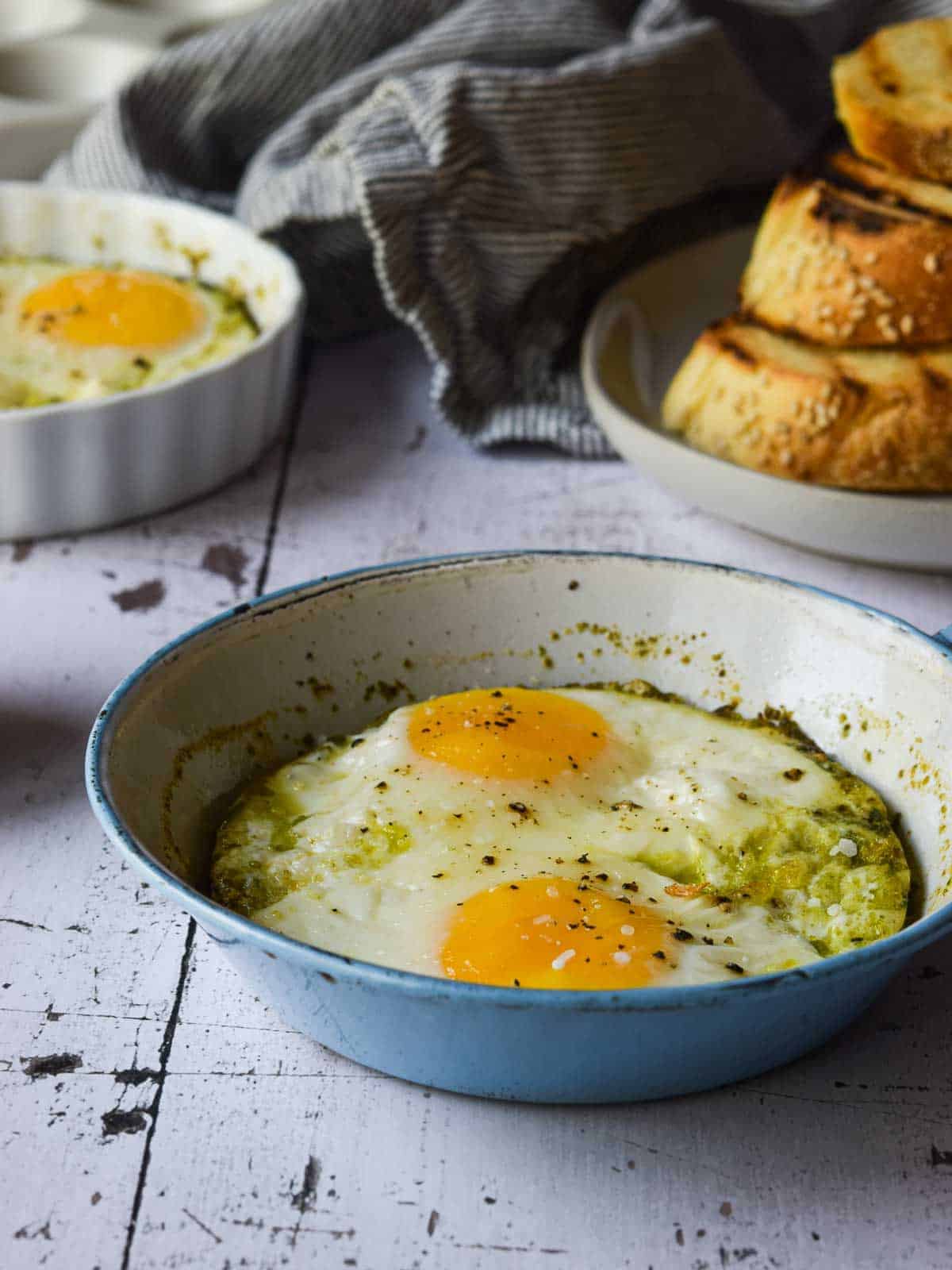 Pesto baked eggs in a blue skillet on a white surface.