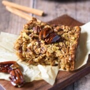Baked pecan pie oatmeal on a wood slab with cinnamon sticks in the background.