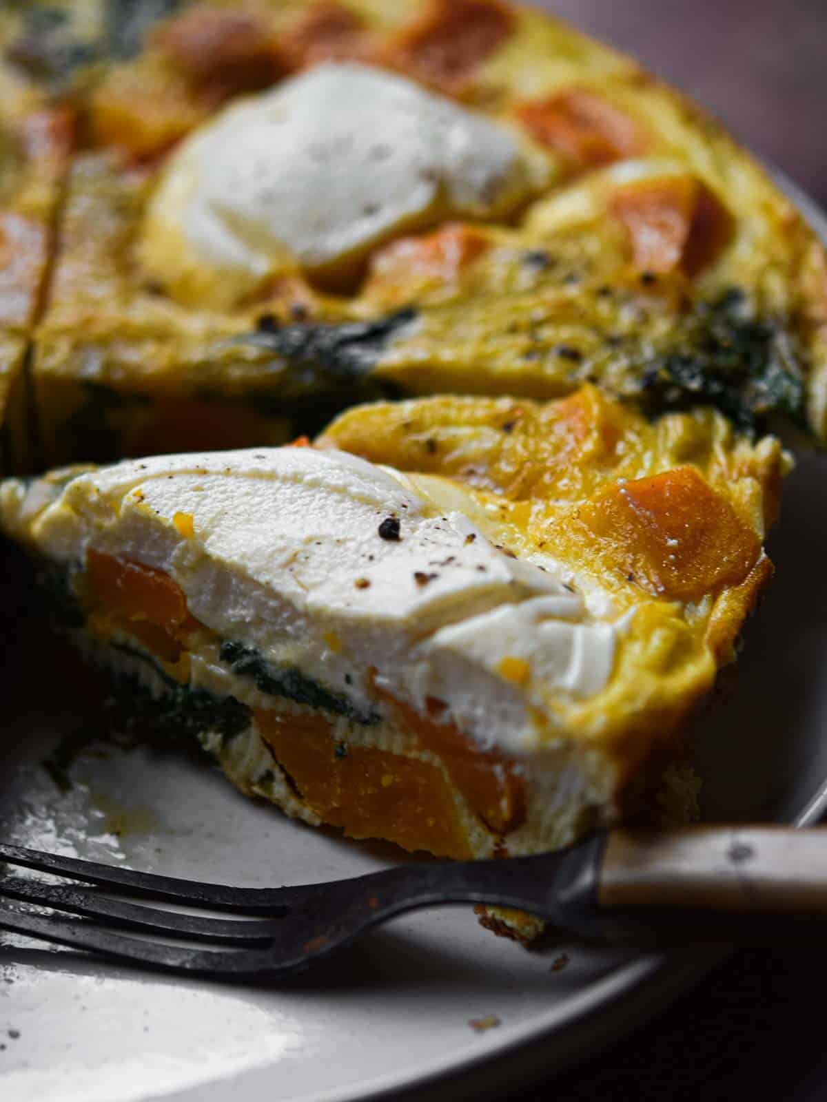 Close-up of a slice of butternut squash frittata cut on a plate with a fork.