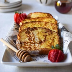 Buttermilk French toast layered on a white plate with strawberries.