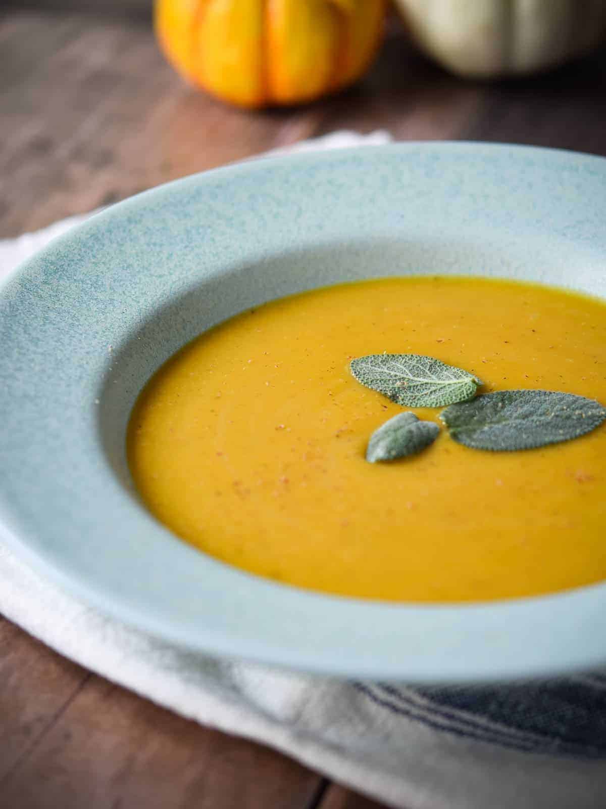 Butternut squash soup in a blue bowl with sage.