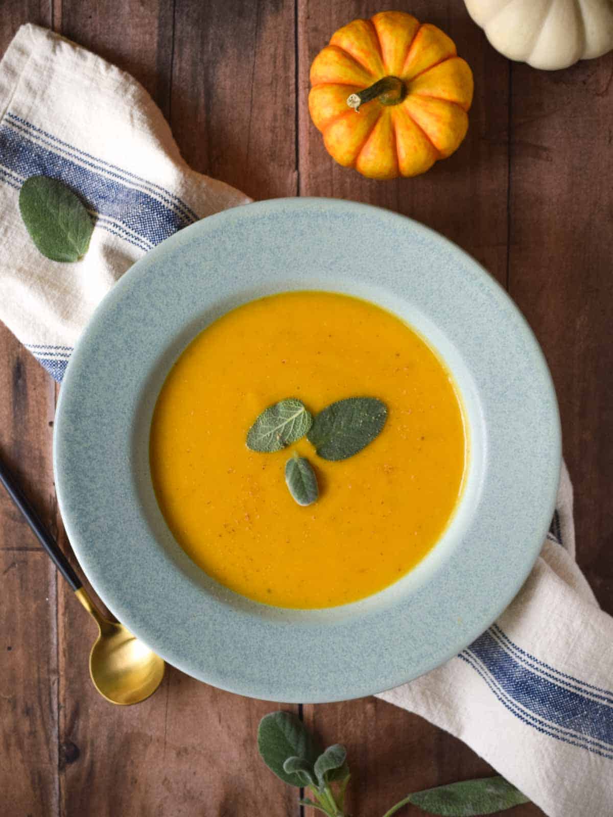 Overhead of squash soup in a blue bowl on a wood background.