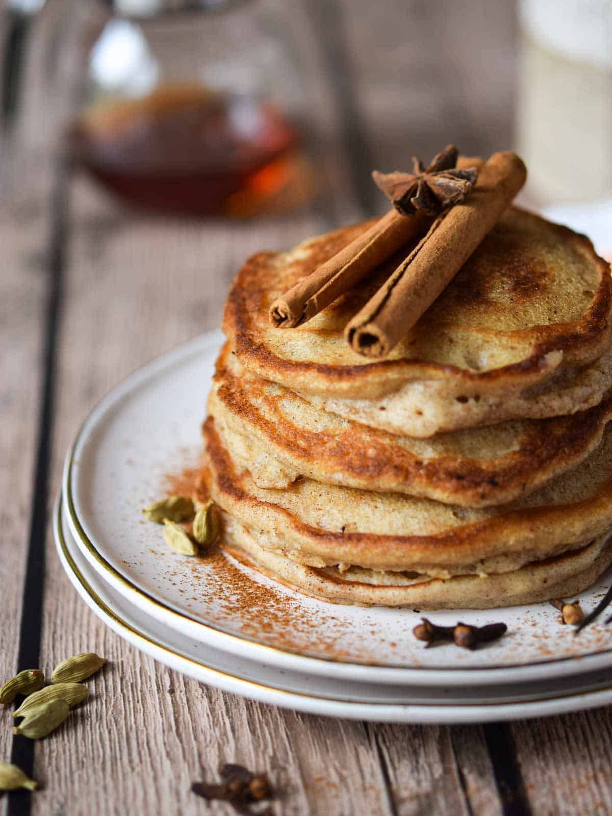 Close-up of pancakes on a plate with cinnamon sticks and spices on top.