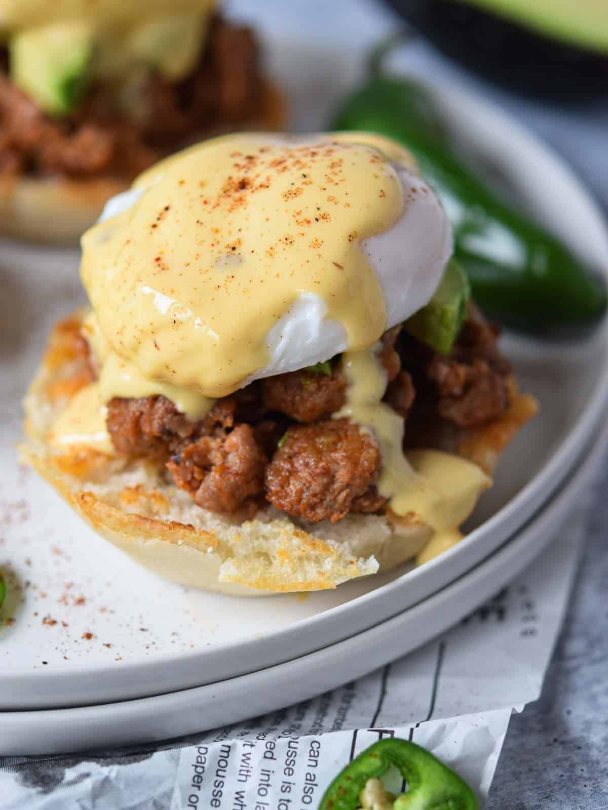 Mexican eggs benedict on a white plate with a jalapeno in the background.