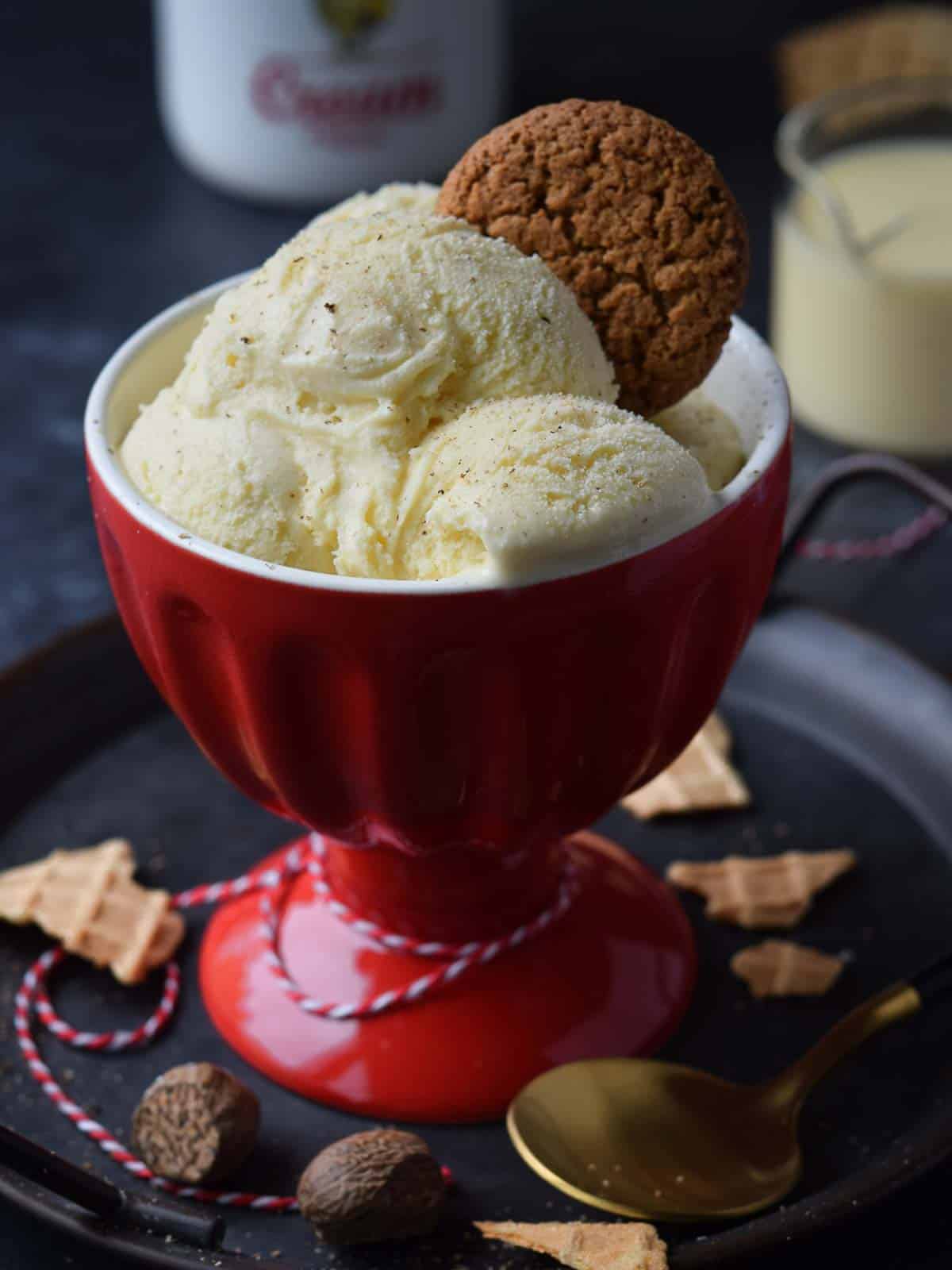 Three scoops of eggnog ice cream in a red cup with a gingersnap on top.