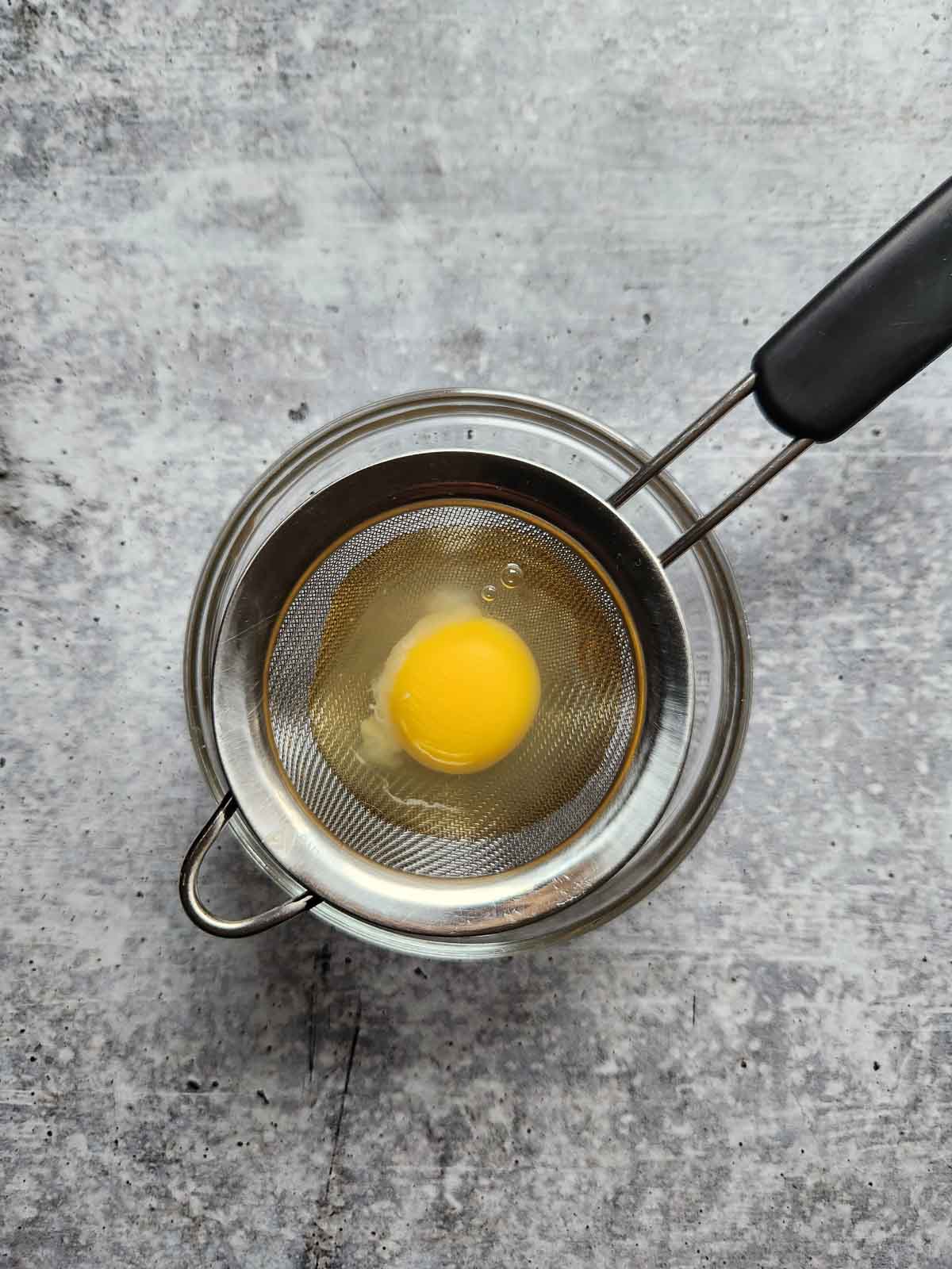 Ann egg in a small strainer over a clear bowl.