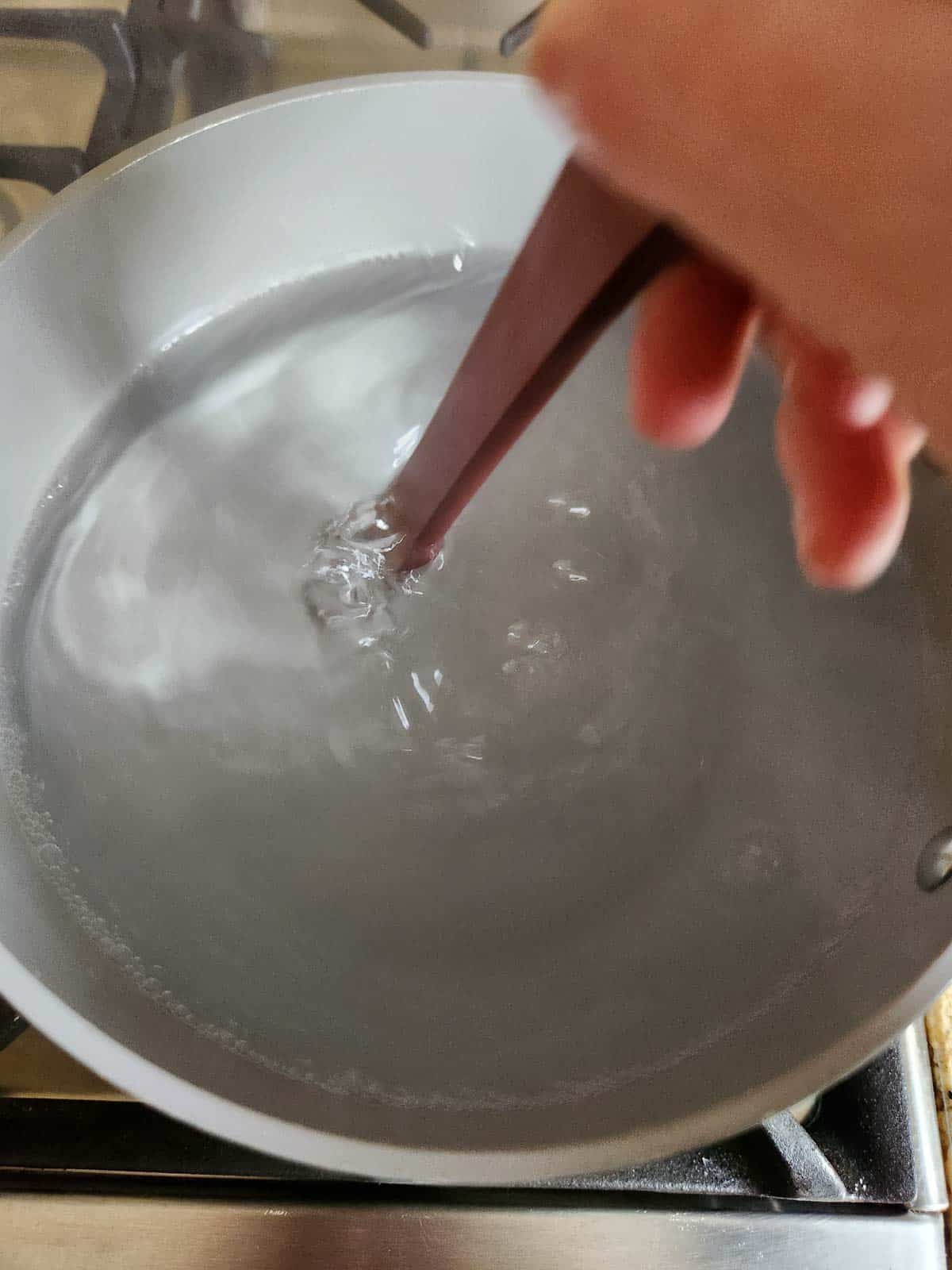 Pot of water being stirred on the stove.