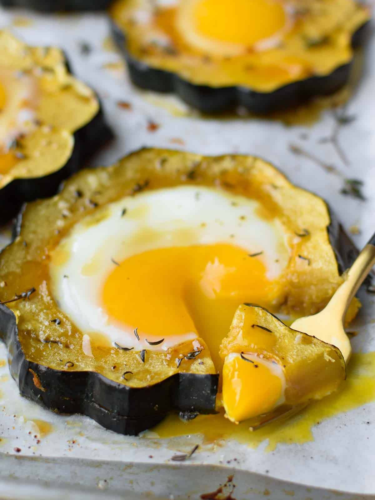 Angled view of acorn squash egg in a hole with a fork bit taken out and dripping yolk.