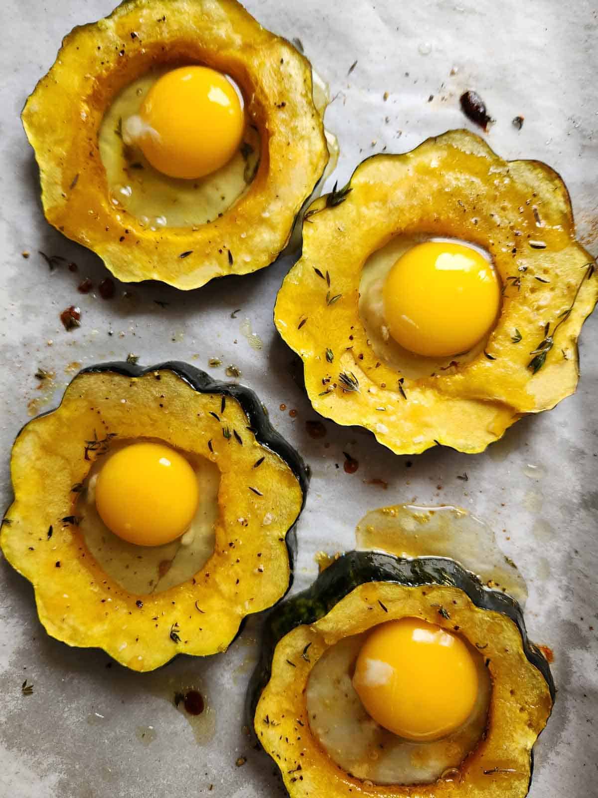 Four acorn squash rings with an uncooked egg in each hole on a baking sheet.