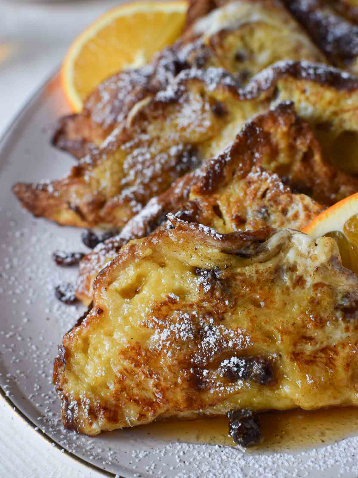Panettone French toast on a beige platter with maple syrup and orange.