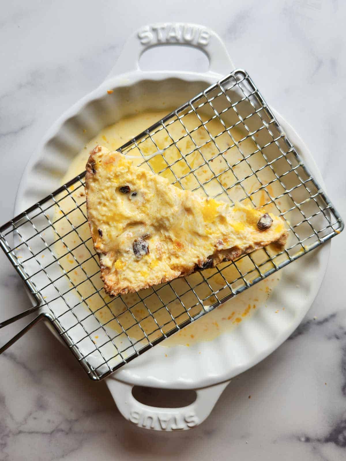 Panettone dipped in custard with excess dripping off in a white plate.