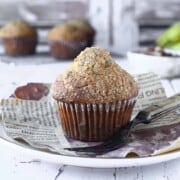 Close-up of a banana muffin on a white plate with muffins in the background.