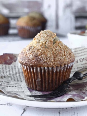 Close-up of a banana muffin on a white plate with muffins in the background.