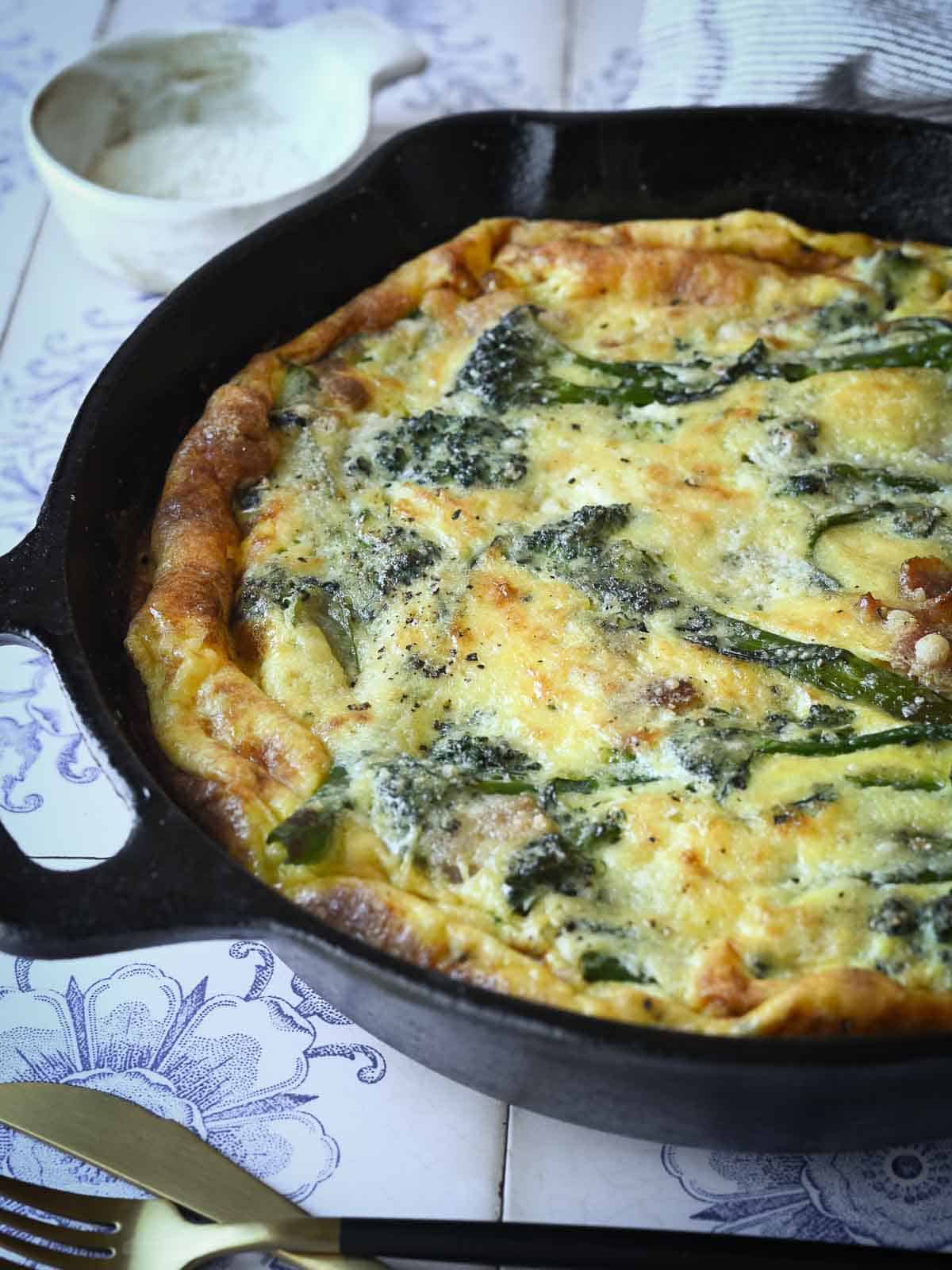 Close-up of broccolini frittata in a skillet on a flowered tile surface.