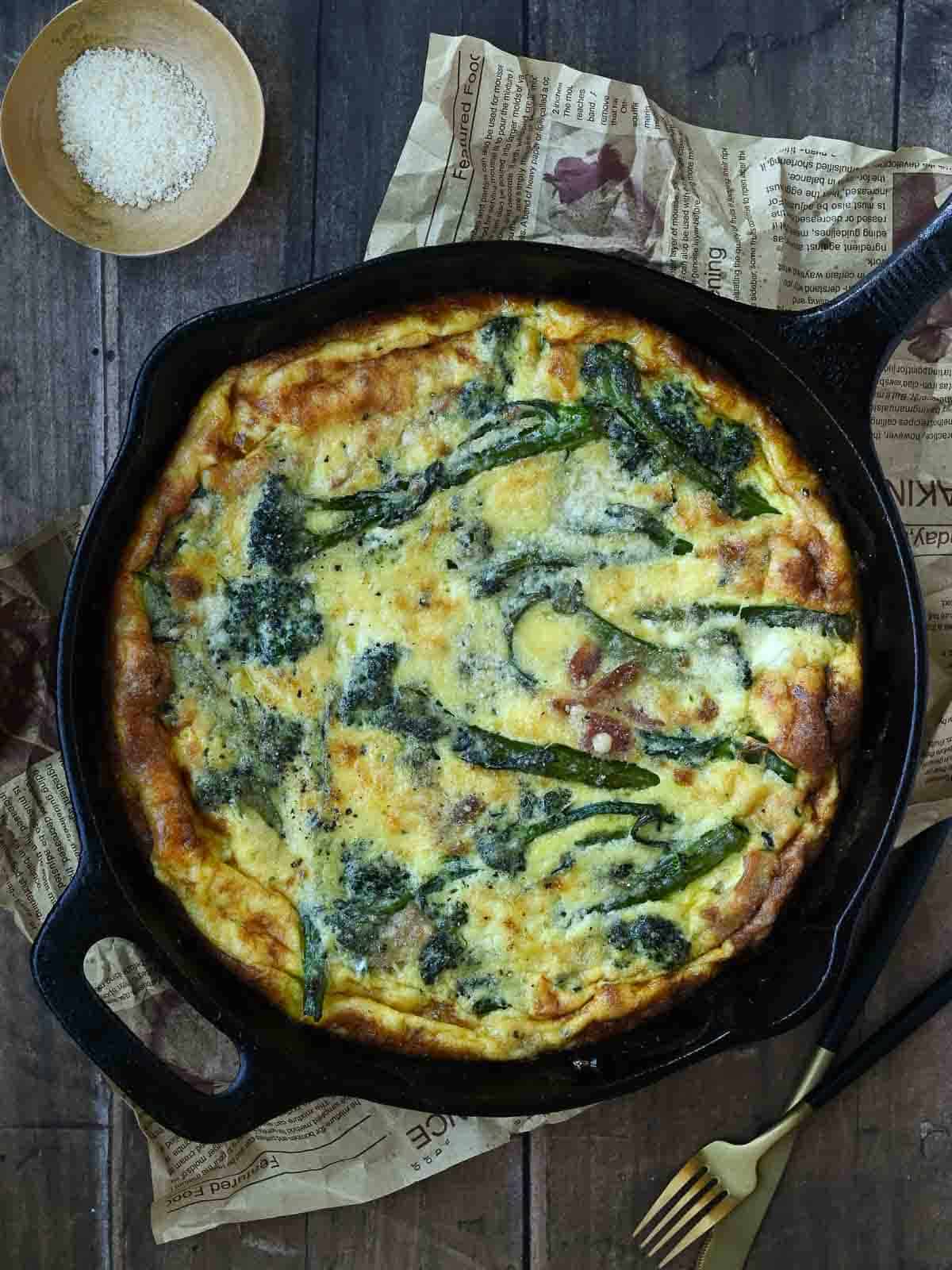 Overhead view of broccolini frittata in a black skillet on a wooden surface.