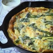 Close-up of broccolini frittata in a skillet with parmesan cheese in the background.