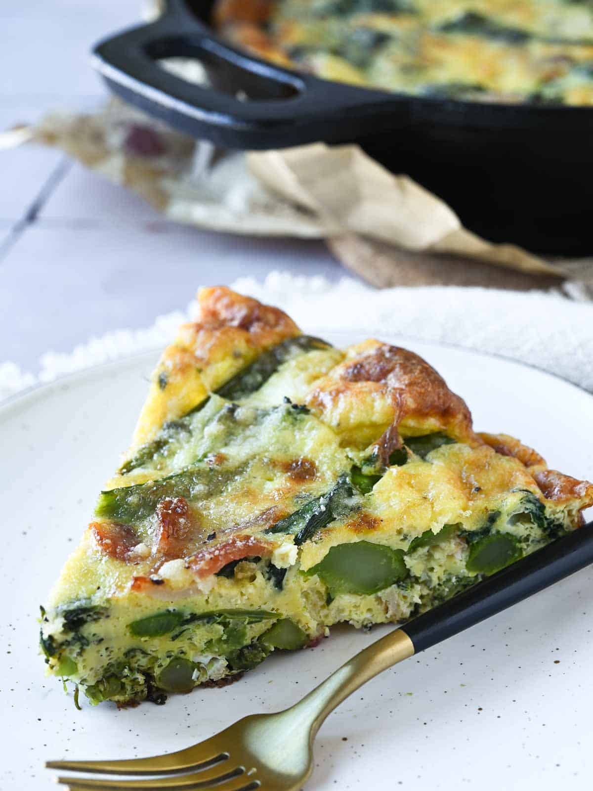 A slice of broccolini frittata on a beige plate with a fork next to it.