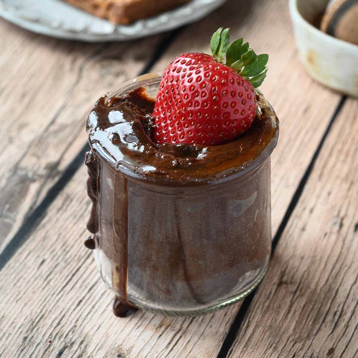 Chocolate tahini spread in a clear jar with a strawberry dipped in.