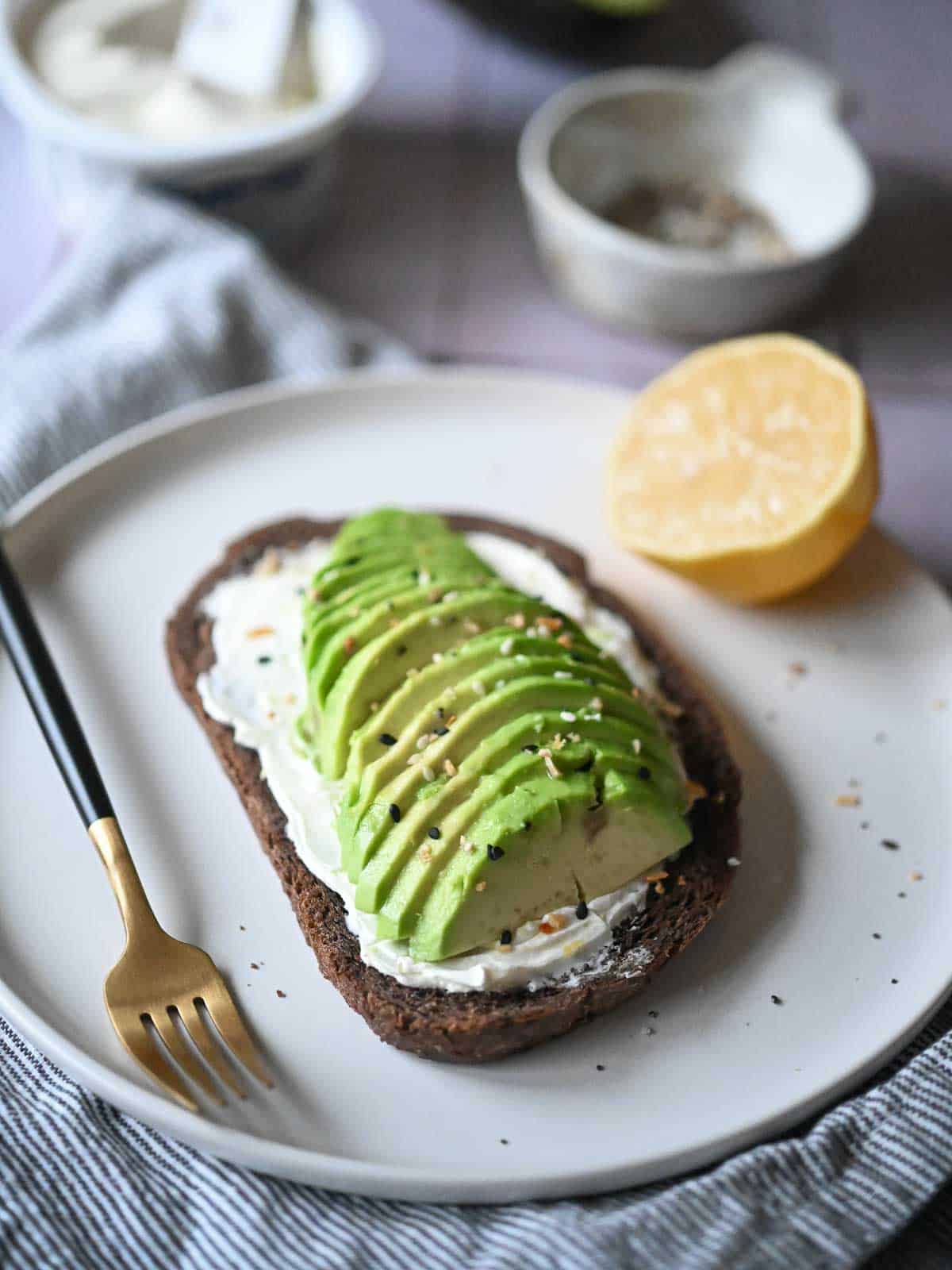 Sliced avocado on pumpernickel bread with cream cheese and spices.
