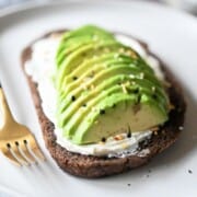 Close-up of sliced avocado on pumpernickel bread with cream cheese and spices.