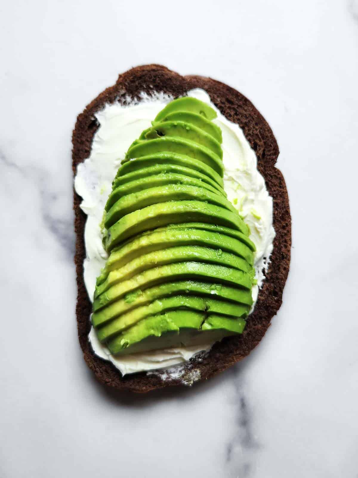 Pumpernickel bread with cream cheese and avocado on a white background.