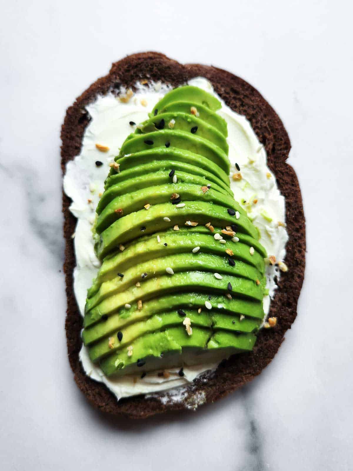 Cream cheese and avocado toast with spices on top on a white background.