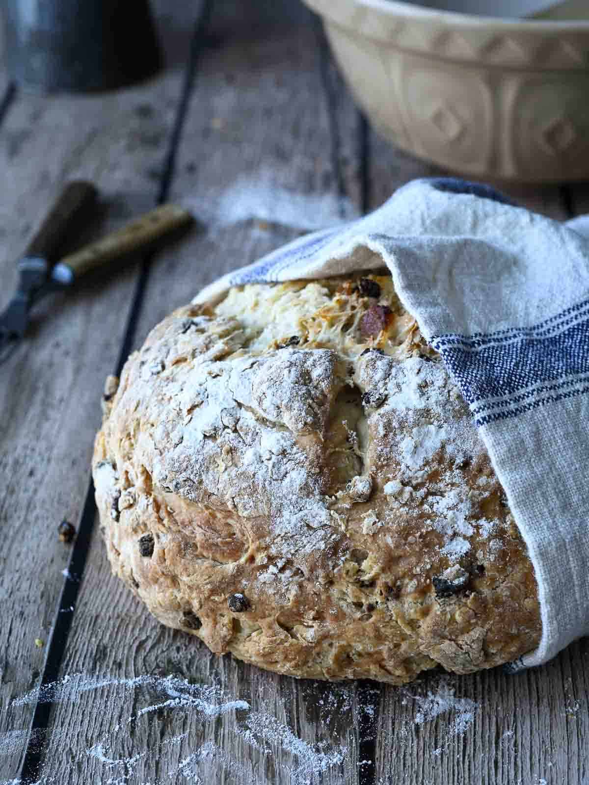 Irish soda bread loaf wrapped in a beige and blue towel on a wood surface.