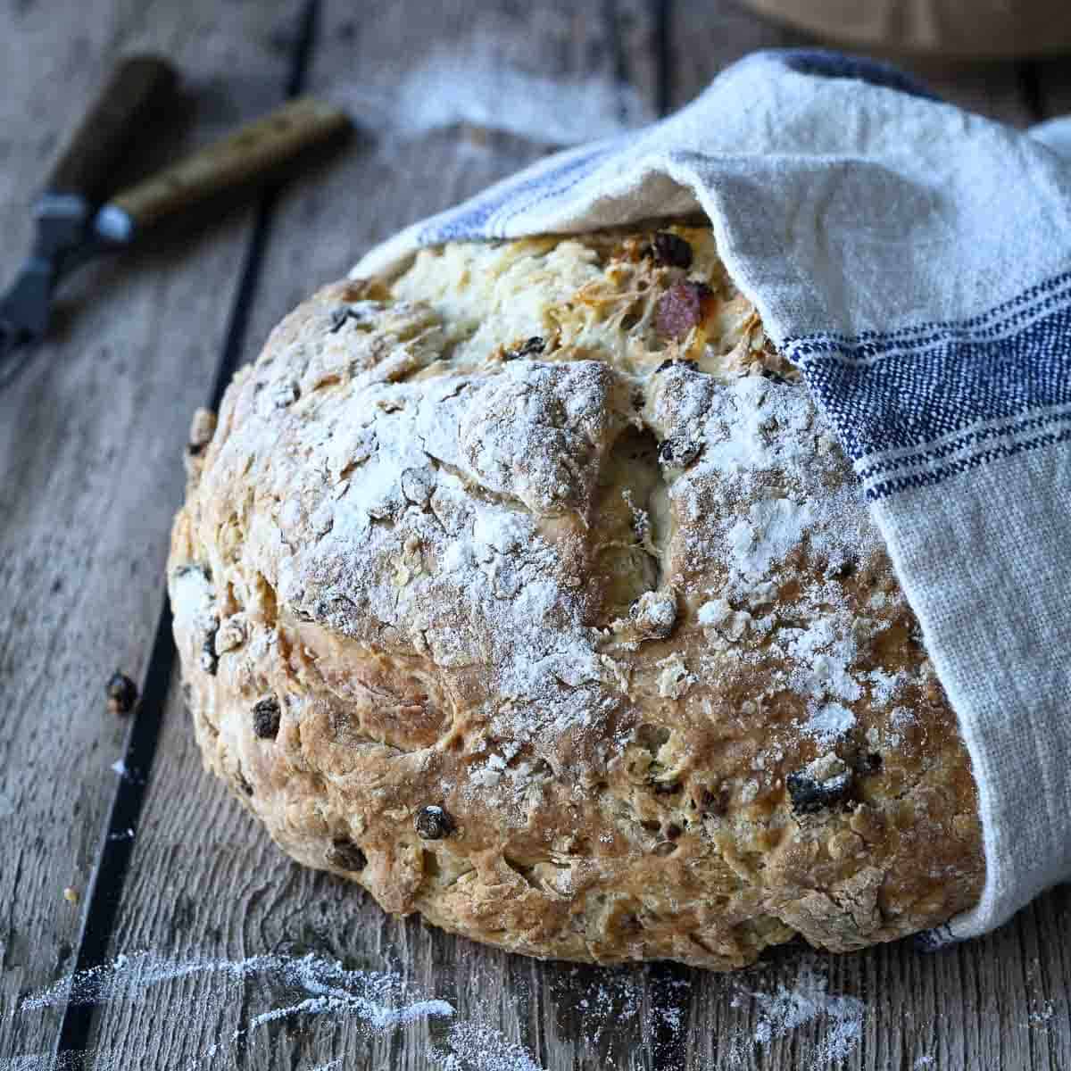 Irish soda bread wrapped in a towel on top of a wooden surface.