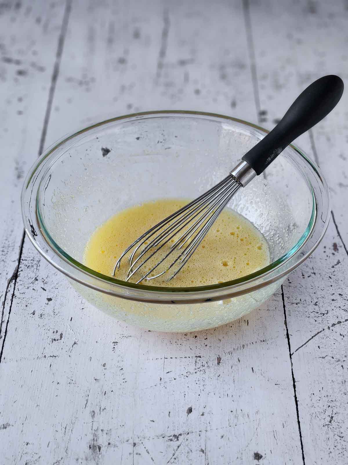 Sugar and eggs mixed together in a clear bowl with a whisk.