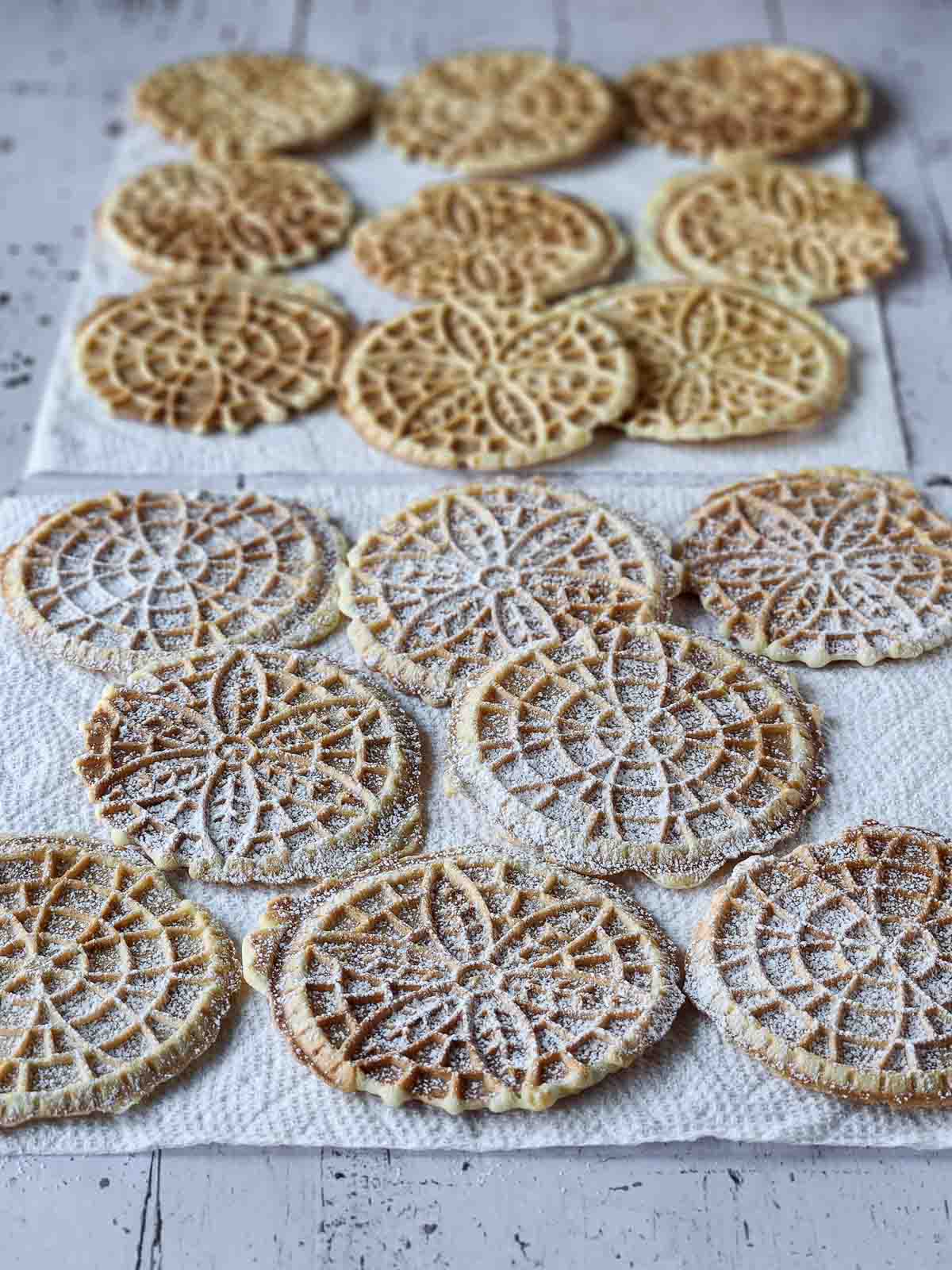 Cooked lemon pizzelles on paper towels with powdered sugar on them.